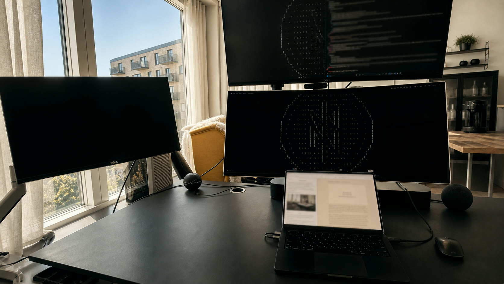 Real workstation with stacked monitors, a laptop, terminal windows, and a lived-in desk beside Copenhagen windows. A practical place for assembling governed agents.