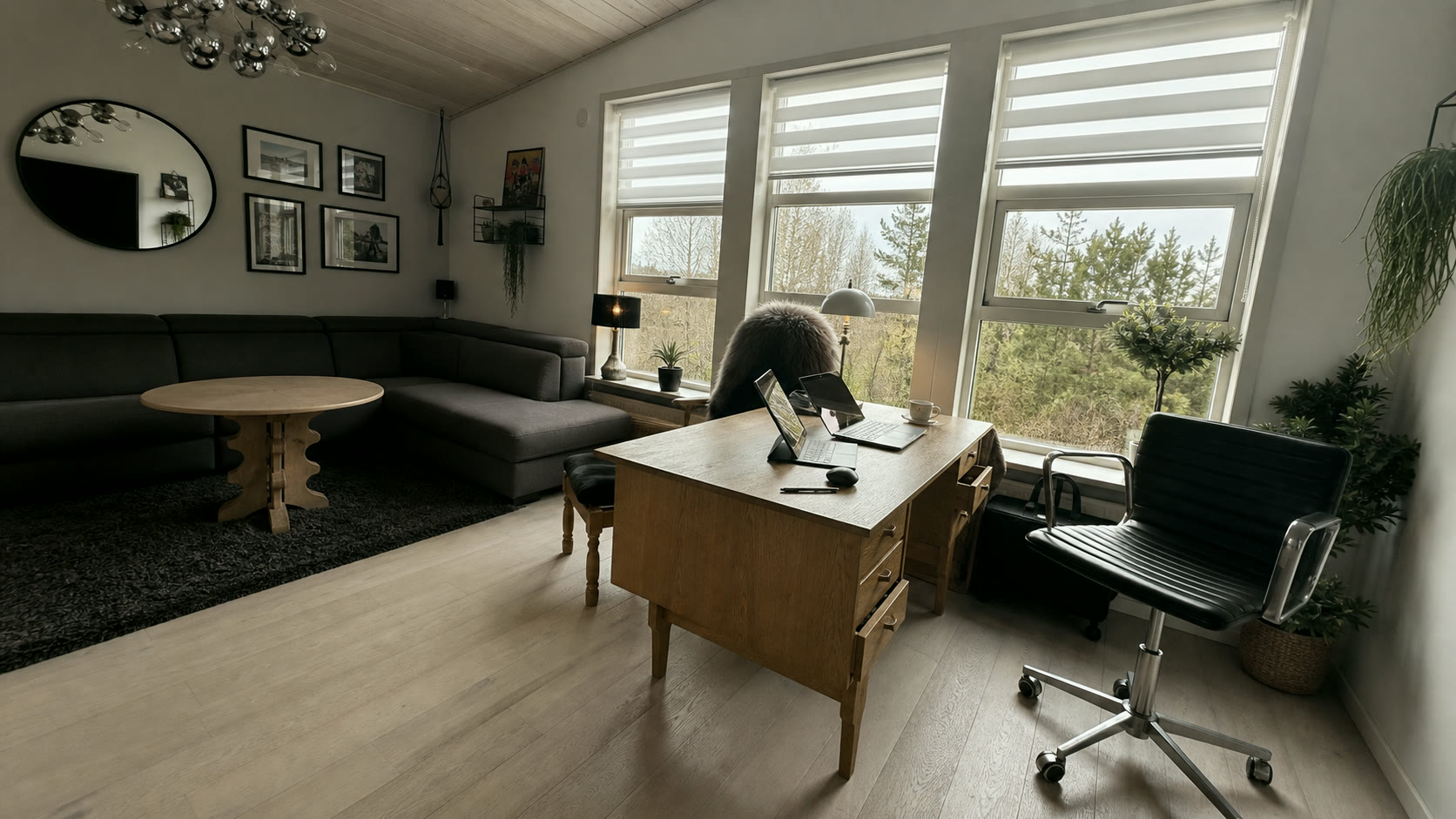 Real Faroese office interior with a wooden desk, sofa, plants, and wide windows looking out to trees under overcast light. A real place where thinking happens.
