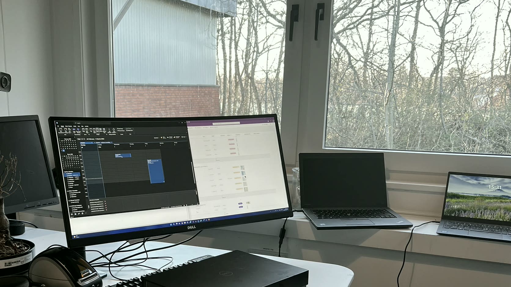 Bright workstation beside large windows, with local screens inside and trees outside. The workbench stays inside its own boundary.